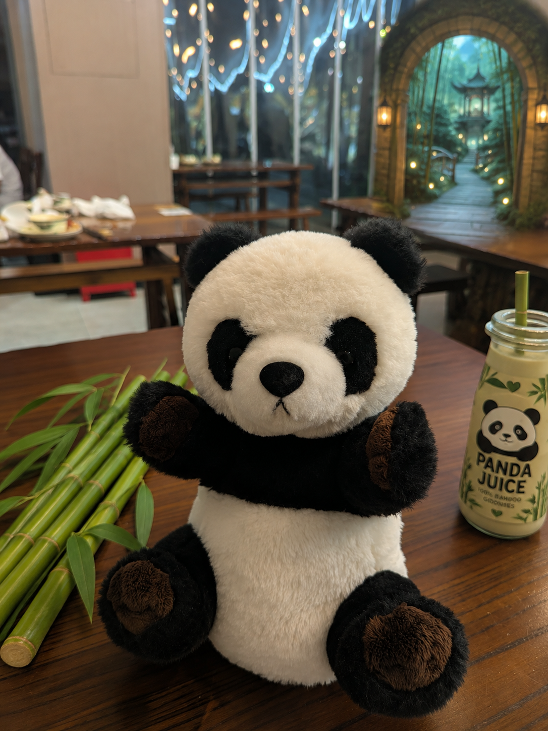 Image returned by ChatGPT: the toy panda on a table with bamboo stalks, a bottle labelled Panda Juice and an archway into a bamboo garden in the background.